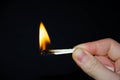 A hand holds a burning match on a black background. A wooden match burns in the hands of a macro. Igniting a match on a box. Smoke Royalty Free Stock Photo