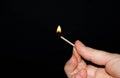 A hand holds a burning match on a black background. A wooden match burns in the hands of a macro. Igniting a match on a box. Smoke