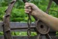 Hand holds a chain of iron and a hammer near a large iron wheel