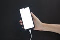 Hand holds a charging smartphone with a light screen on a black background Royalty Free Stock Photo
