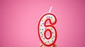 Hand holds colorful number 6 birthday cake candle on a pink back