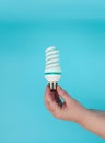 The hand holds a compact spiral-type fluorescent lamp with an E27 base on a blue background. Royalty Free Stock Photo