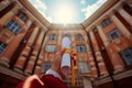 A hand holds a diploma in front of a grand building under a sunny sky