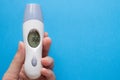 Hand holds electronic thermometer on a blue background