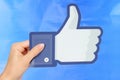 Hand holds Facebook logo on blue paper background