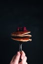 Hand holds a fork with juicy pancakes with berries and honey