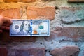 A hand holds a hundred dollar bill against the background of an old brick wall close-up. Old crumbling red brick wall and cash, us