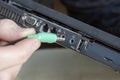 Hand holds and inserts the green cinch plug into the socket for the headphones in the laptop.