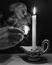 A hand holds a lit match after lighting a candle, with a cloud of smoke in the dark background Royalty Free Stock Photo