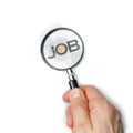 A hand holds a magnifying glass while examining the word JOB. Job search concept