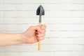 hand holds miniature gardening tool against a white brick wall. shovel in a woman's hand Royalty Free Stock Photo