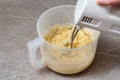 A hand holds a mixer for beating dough in a plastic bowl. Kneading dough in a mixer. Homemade baking concept Royalty Free Stock Photo