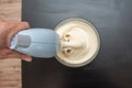 Hand holds a mixer that whips cream in a glass bowl on a dark kitchen table Royalty Free Stock Photo