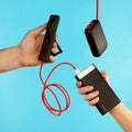 Hand holds mobile phone and powerbank with red charging wire on blue background Royalty Free Stock Photo