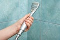 Shower head in human hand on background of tiles in bathroom