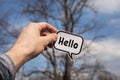 A hand holds a paper cloud with the word hello on the background of trees