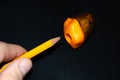 A hand holds a pencil and sharpens in a sharpener. A pencil for a pencil on a black background. Orange pencil, orange chink,