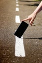 The hand holds the phone, which is on the road, on the dividing strip