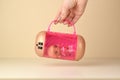 Hand holds pink container with plastic LOL doll on table. LOL Surprise series toys manufactured by MGA Entertainment inc