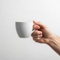 A hand holds a plain white ceramic cup against a neutral background Royalty Free Stock Photo