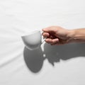 A hand holds a plain, white ceramic cup against a white background Royalty Free Stock Photo