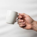 A hand holds a plain white ceramic mug against a white background Royalty Free Stock Photo