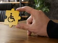 A hand holds puzzle piece with a symbol of a Disabled person. Inclusive workplace concept. Royalty Free Stock Photo