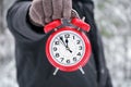 Hand holds a red alarm clock showing 12 o`clock