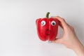 Hand holds red bell paprika with Googly eyes and frightened funny face. Raw sweet pepper on white background Royalty Free Stock Photo