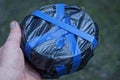 Hand holds a round box in black cellophane wrapped in blue electrical tape