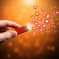 A hand holds a small, rectangular red device emitting social media icons, such as hearts Royalty Free Stock Photo