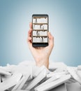 A hand holds a smartphone with a book shelf on the screen. A heap of books with white covers. A concept of education and technolog Royalty Free Stock Photo