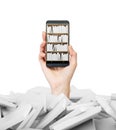 A hand holds a smartphone with a book shelf on the screen. A heap of books with white covers.