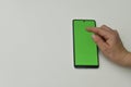 hand holds smartphone with green screen and simultaneously taps on display with one finger. Royalty Free Stock Photo