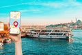 A hand holds a smartphone with an online maps app. In the background, a river with a tourist ship. Concept of travel, cruises and Royalty Free Stock Photo