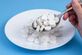 A hand holds a spoon over a plate of pills on a blue background. Pill overdose concept. The use of food additives Royalty Free Stock Photo