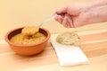 Hand holds spoonful of soup with bread roll and napkin on table