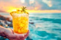 Hand holds a tropical pineapple cocktail against a sunset seascape