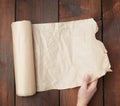 Hand holds unfolded roll with brown parchment paper on wooden background Royalty Free Stock Photo