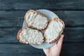 Hand holds white plate with homemade sandwiches with cream-cheese over a black wooden table.