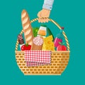 Hand holds wIcker picnic basket full of products.