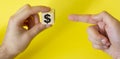 Hand holds a wooden cube with a dollar sign and points a finger at it on a yellow background Royalty Free Stock Photo