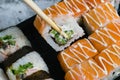 Hand holds wooden sticks sushi california roll with fish, cheese and mayonnaise. Large set of rolls on the background Royalty Free Stock Photo