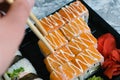 Hand holds wooden sticks sushi california roll with fish, cheese and mayonnaise. Large set of rolls on the background Royalty Free Stock Photo