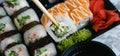 Hand holds wooden sticks sushi california roll with fish, cheese and mayonnaise. Large set of rolls with soy sauce and Royalty Free Stock Photo