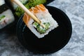 Hand holds wooden sticks sushi california roll with fish, cheese and mayonnaise. Large set of rolls with soy sauce and Royalty Free Stock Photo