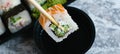 Hand holds wooden sticks sushi california roll with fish, cheese and mayonnaise. Large set of rolls with soy sauce and Royalty Free Stock Photo