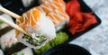 Hand holds wooden sticks sushi california roll with fish, cheese and mayonnaise. Large set of rolls with soy sauce and Royalty Free Stock Photo