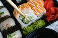 Hand holds wooden sticks sushi california roll with fish, cheese and mayonnaise. Large set of rolls with soy sauce and wasabi on Royalty Free Stock Photo