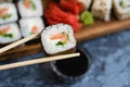 Hand holds wooden sticks sushi roll with spinach, cheese, salmon and nori. Large set of rolls on the background Royalty Free Stock Photo